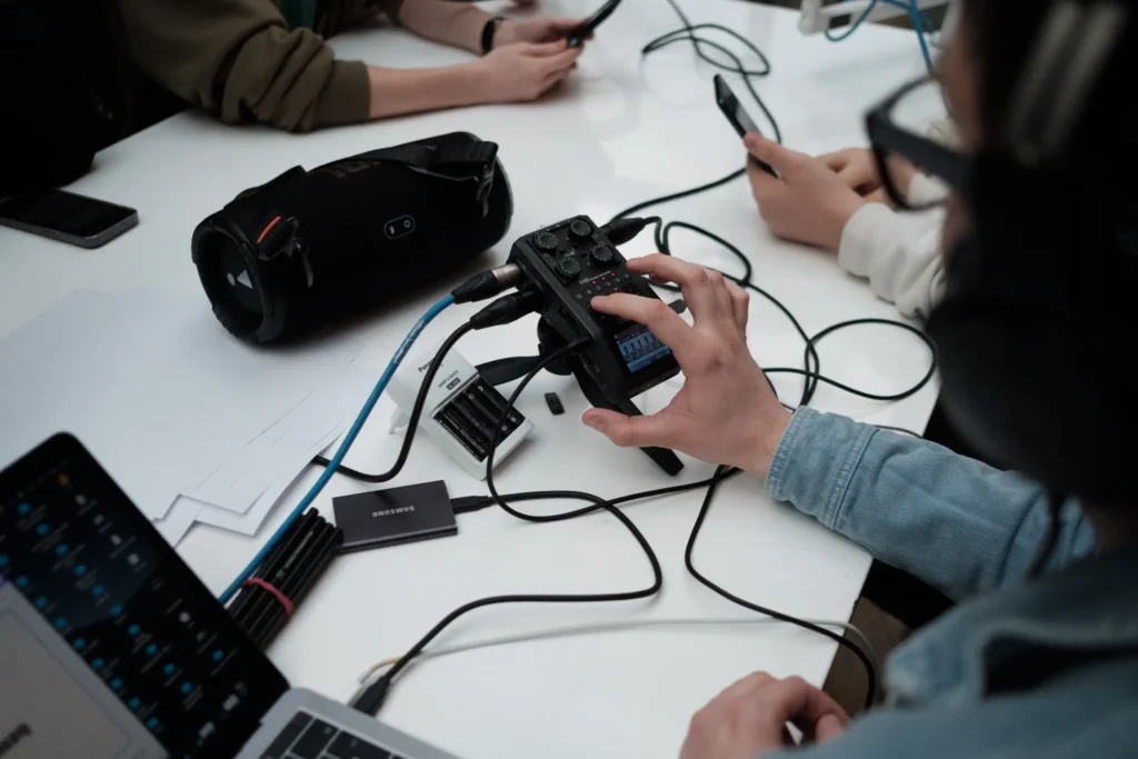 Uczestnik warsztat&oacute;w obsługuje rejestrator dźwięku podczas nagrywania podcastu przy wsp&oacute;lnym stole.